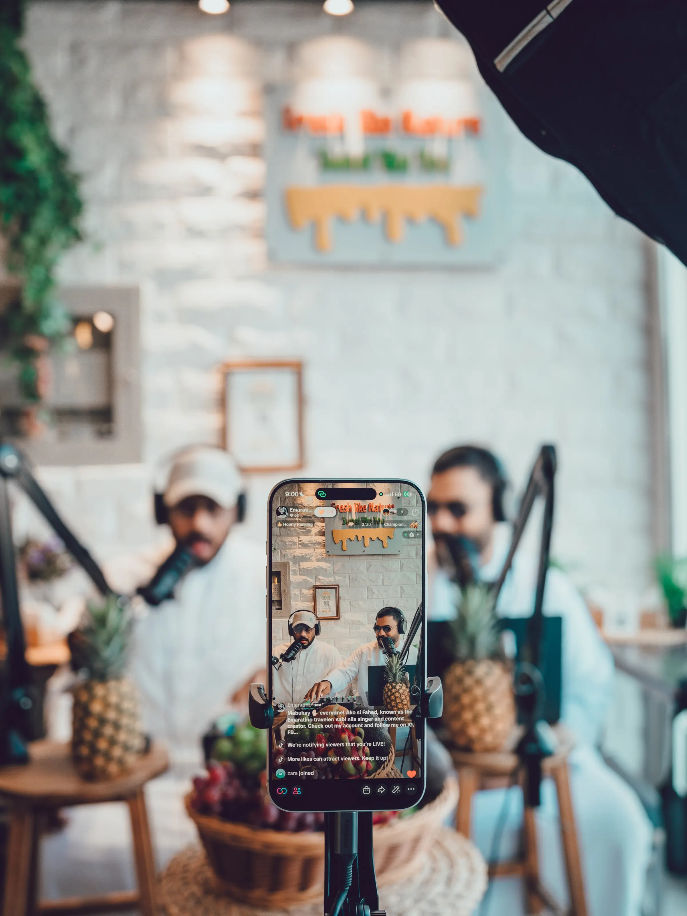 A phone mounted on a rig framing two presenters recording at a podcast set