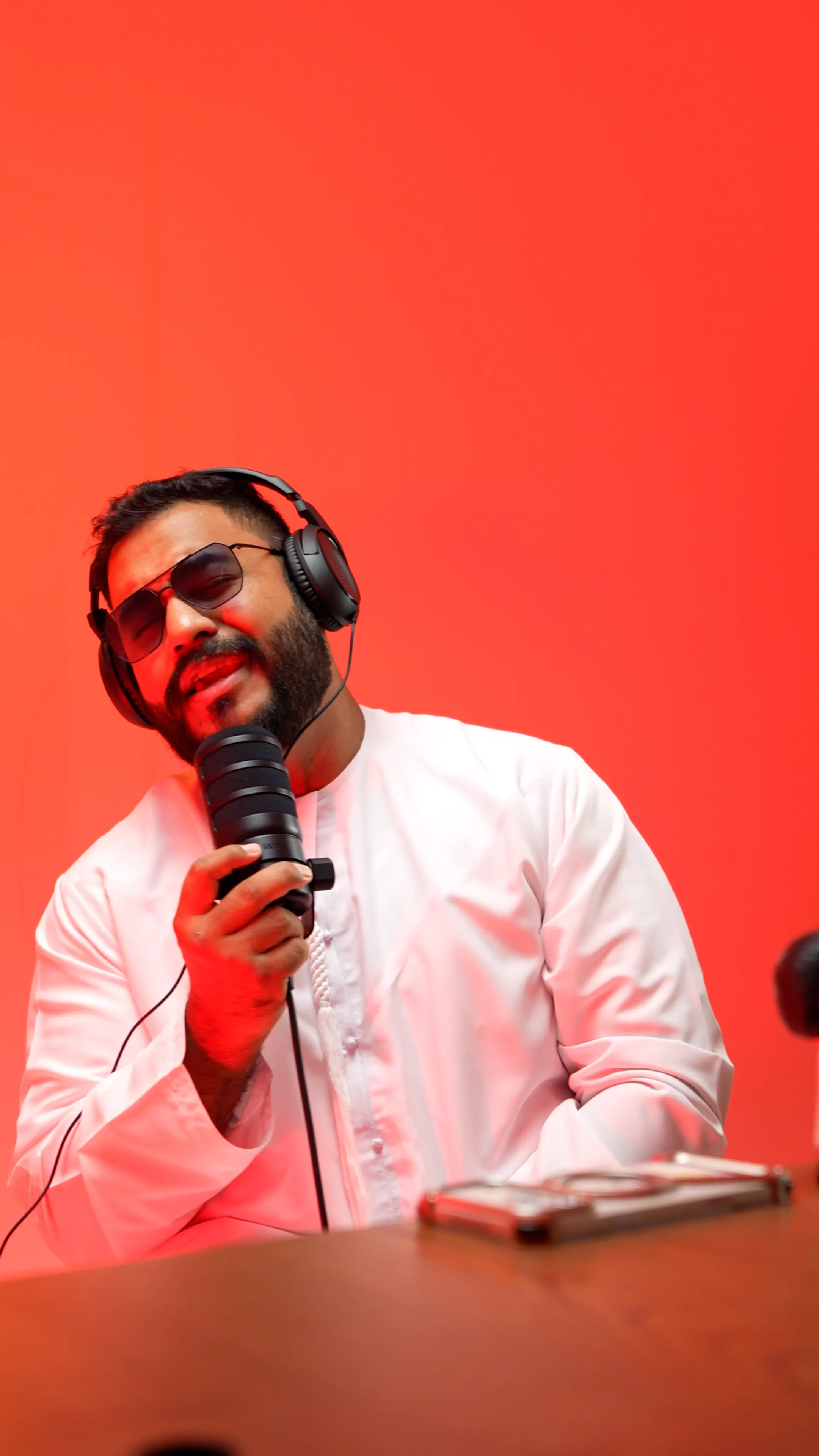 Presenter wearing headphones speaking into a microphone on a red studio set