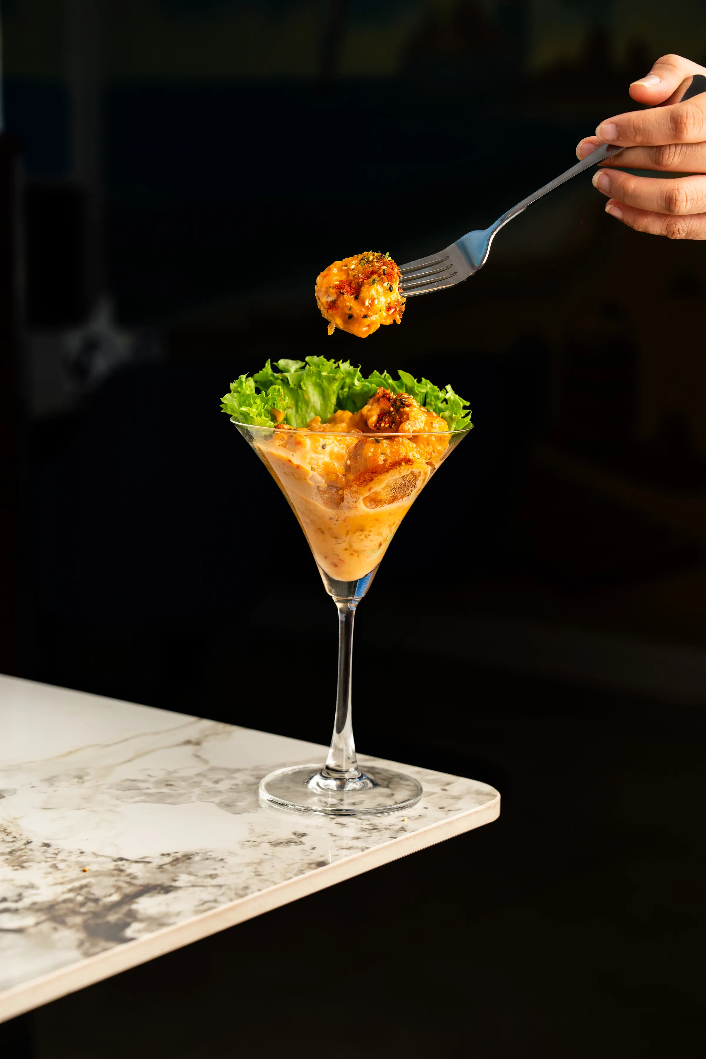 Fork lifting a prawn above a seafood cocktail served in a martini glass on marble