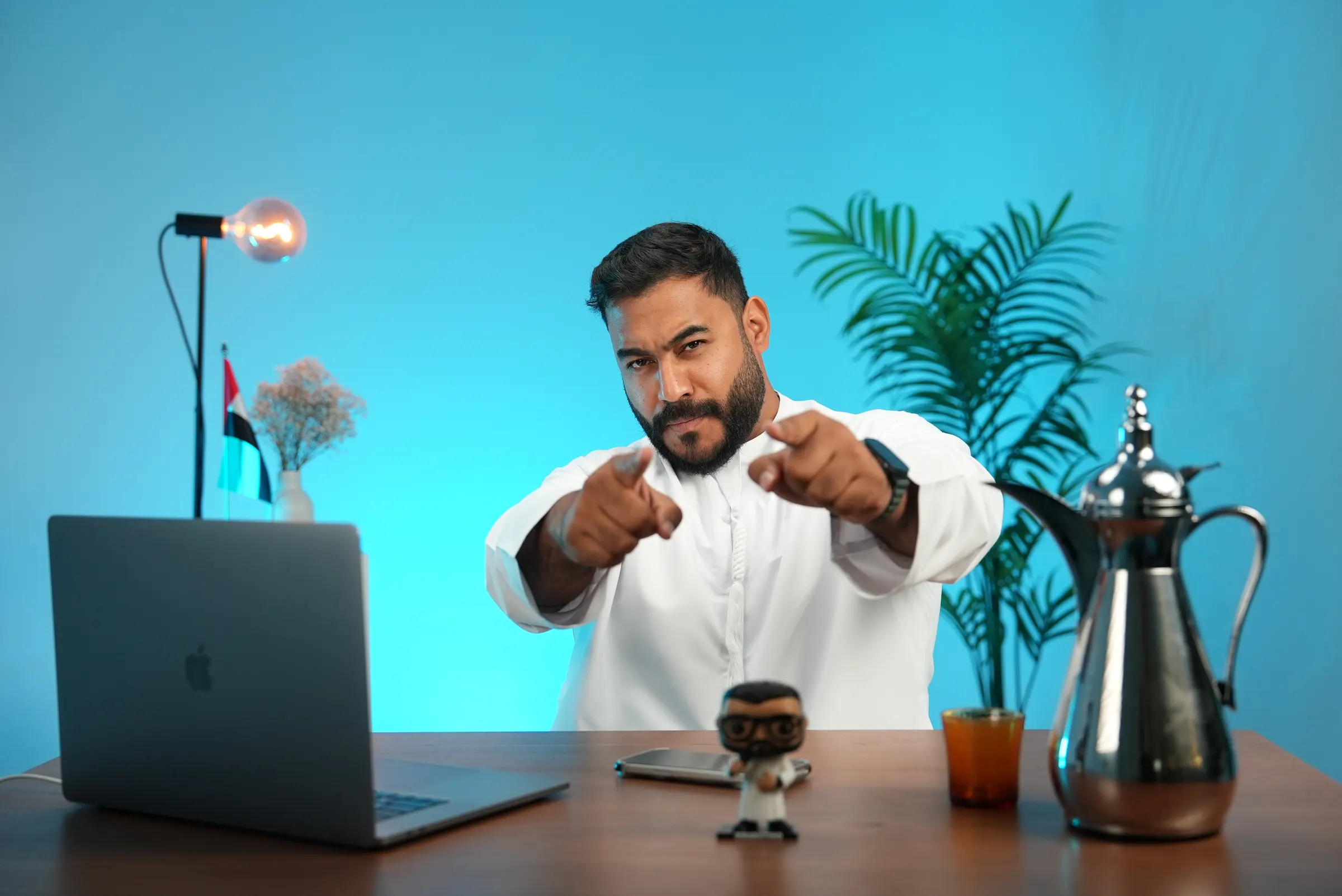 Presenter gesturing to camera at a desk set dressed with an Arabic coffee service