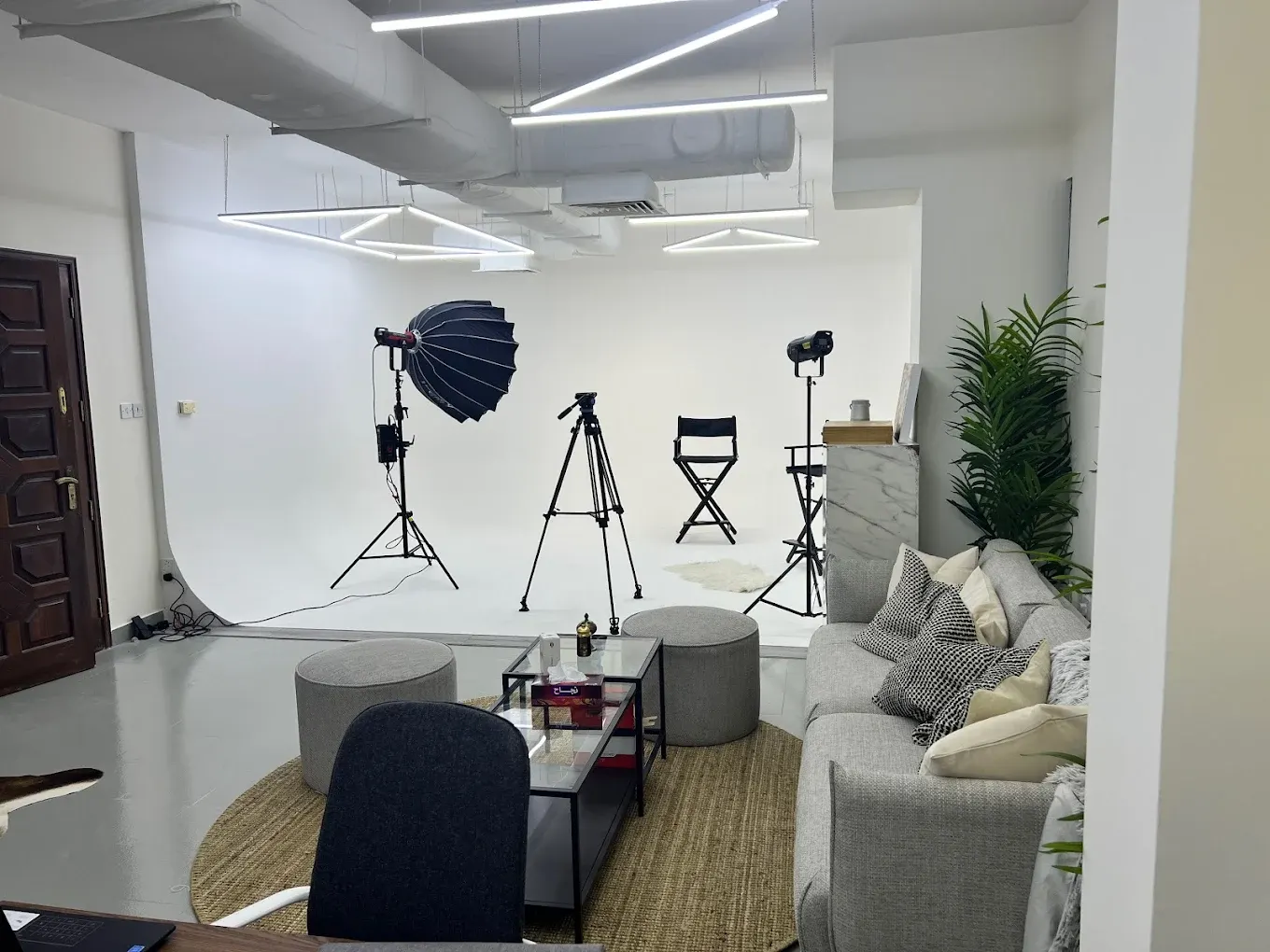 White cyclorama studio with lighting stands, a tripod and a lounge seating area